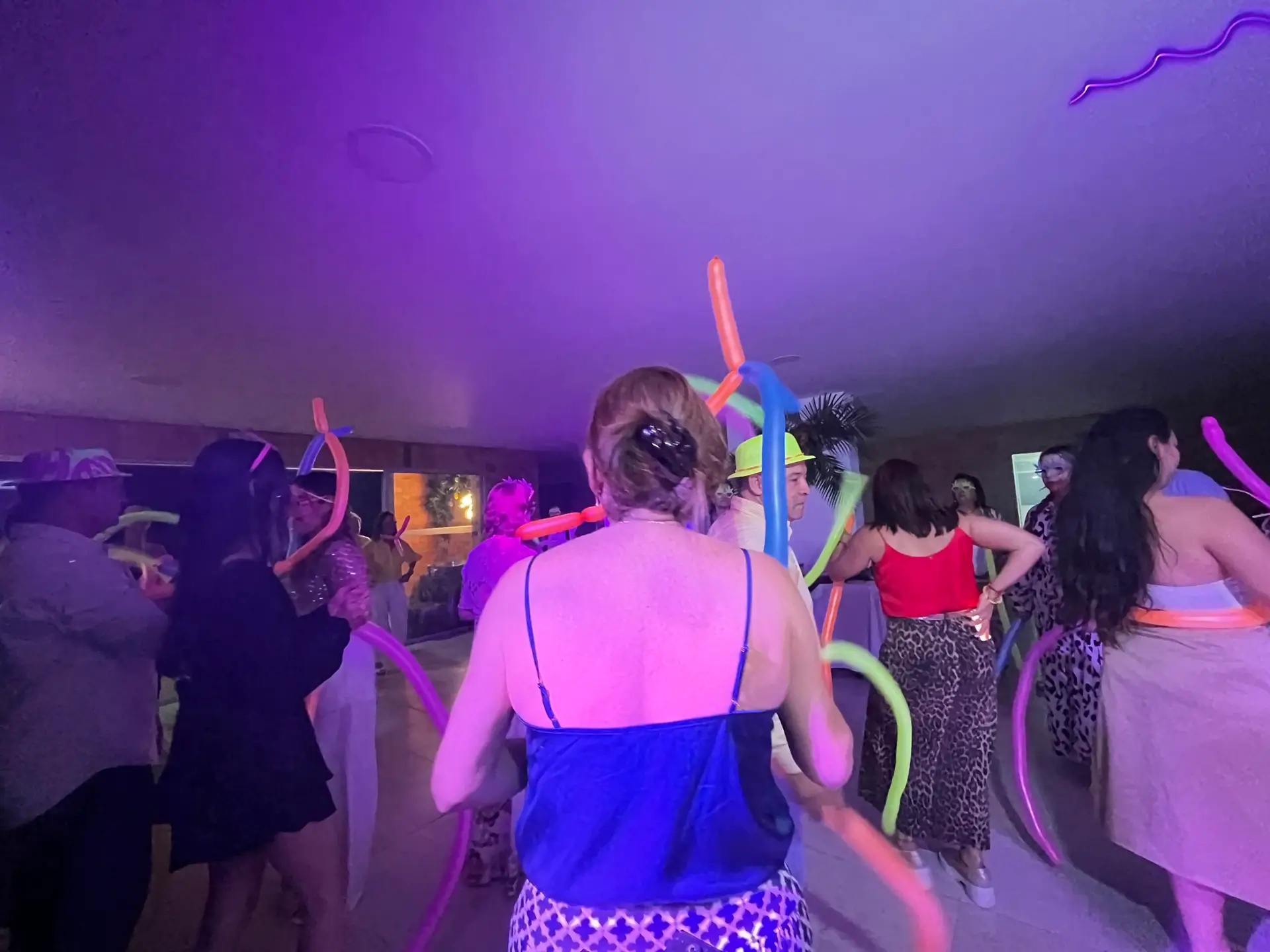 Personas bailando y celebrando con bombas de colores en un salón social en Envigado, música y luces creando un ambiente alegre.