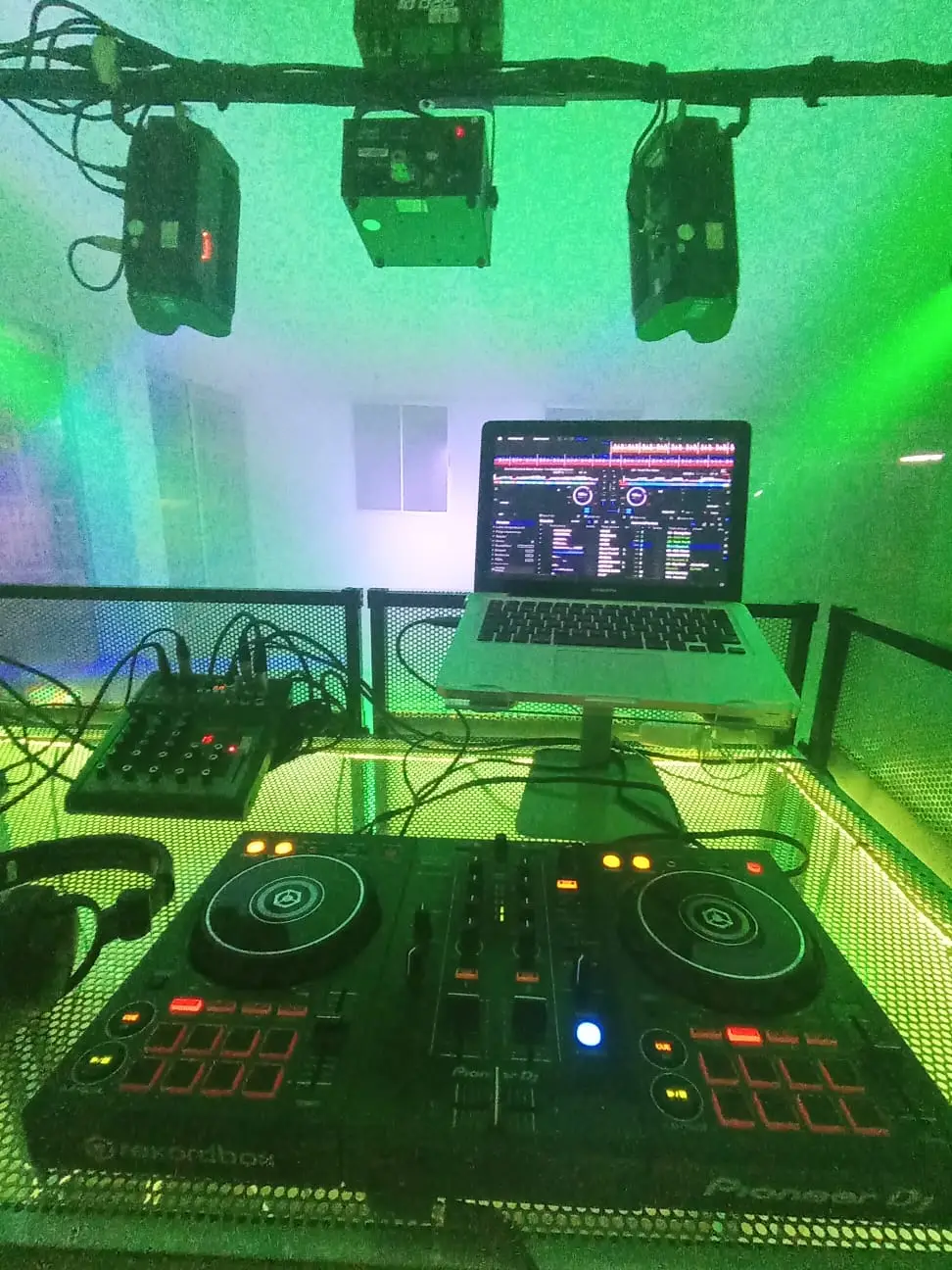 Mesa de DJ con portátil Apple, consola Pioneer, auriculares y luces LED, lista para animar una fiesta especial.